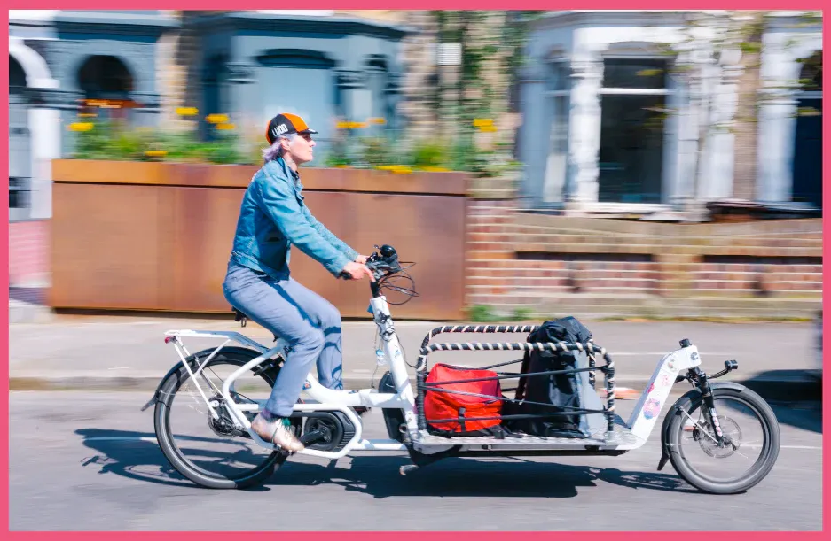 A DabbaDrop rider carrying strapped-down crates on an electric cargo bike along a London street