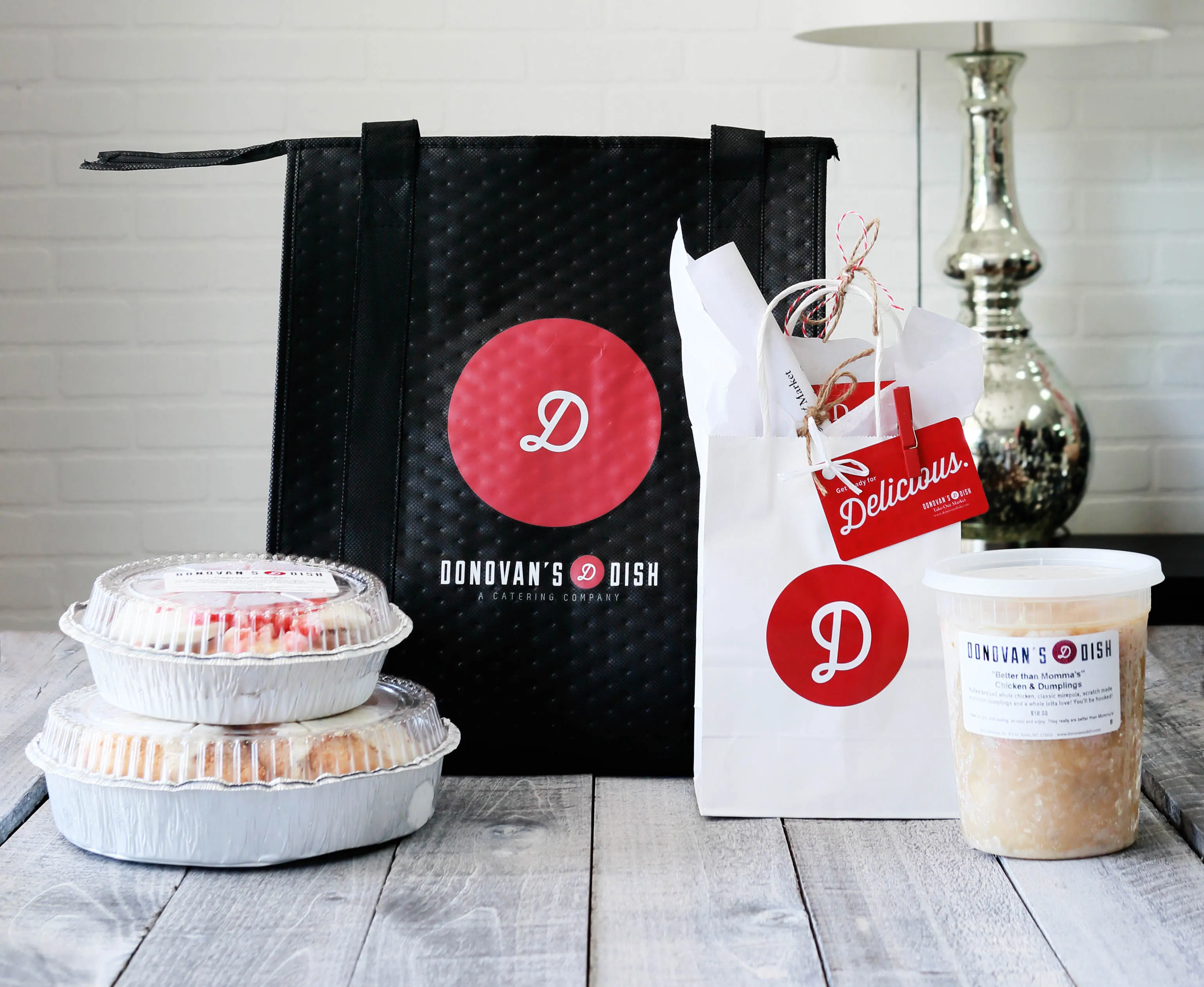 A Donovan's Dish insulated tote and gift bag beside foil pans and a tub of Better than Momma's chicken and dumplings