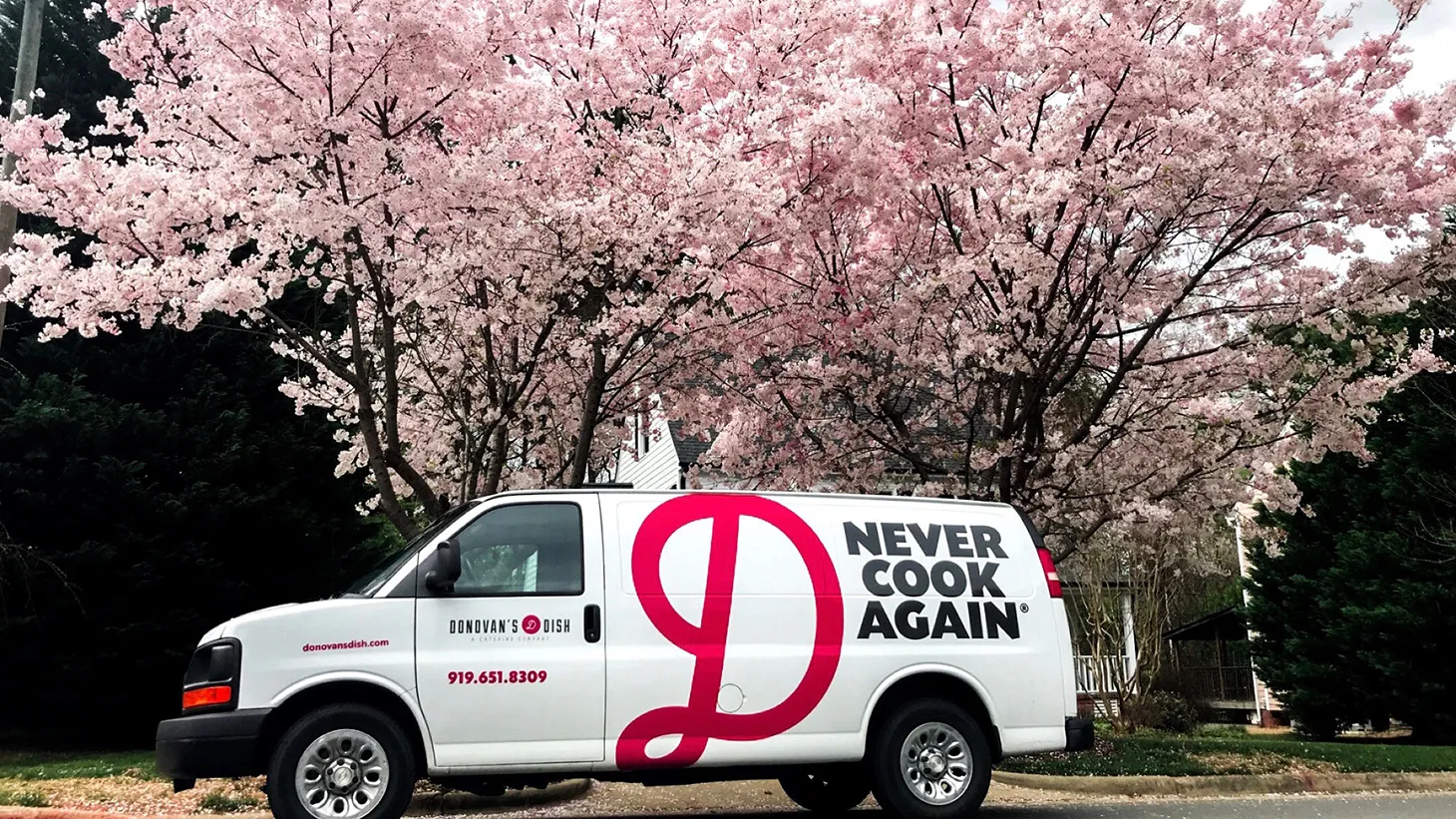 A Donovan's Dish delivery van parked under a cherry tree in blossom, Never Cook Again lettered on its side