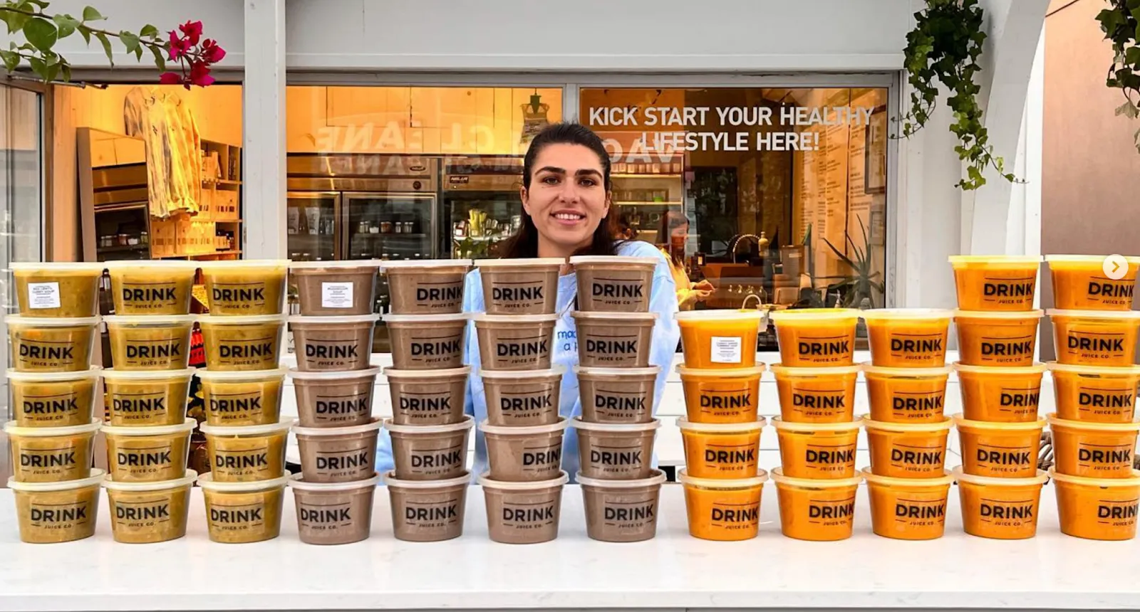 A Drink Juice Co. team member behind a market stall stacked with dozens of branded soup and juice tubs
