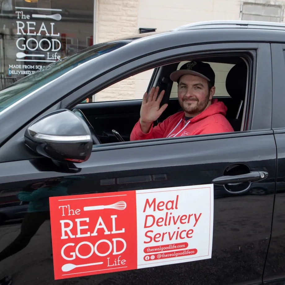 A Real Good Life driver waving from his car, a Meal Delivery Service magnet on the door