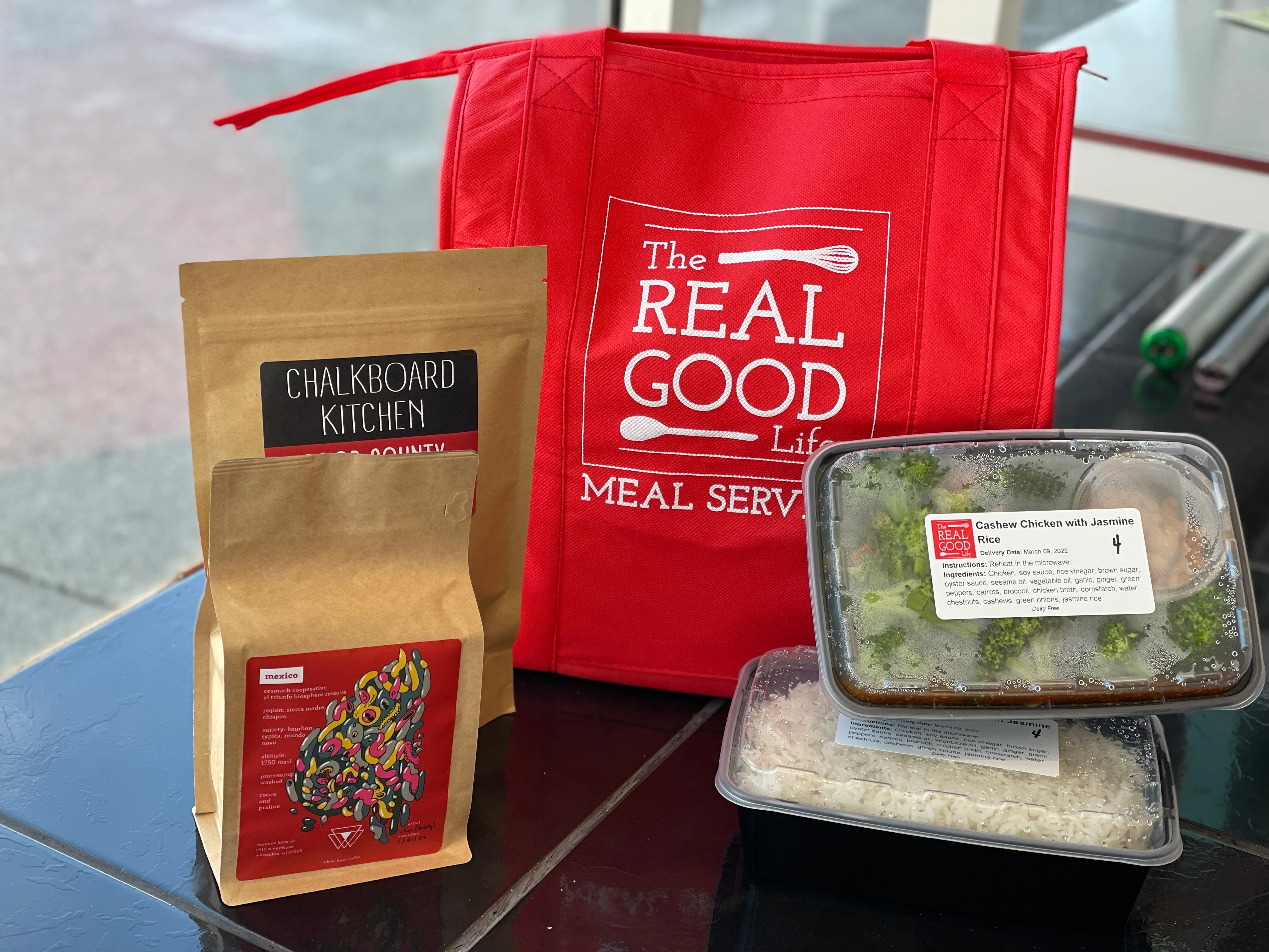 A Real Good Life insulated tote with a bag of Chalkboard Kitchen coffee and a labelled cashew chicken with jasmine rice meal tray